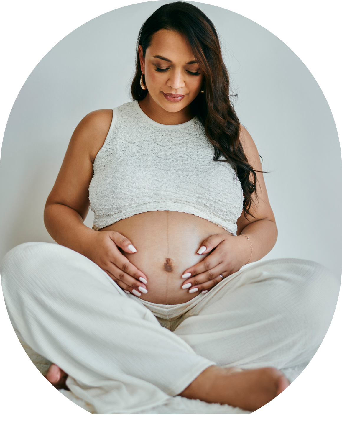 Pregnant woman cradling belly in white attire.